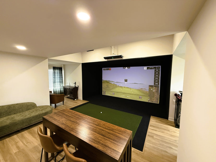 Golf simulator room with tables and chairs for seating behind it. Screen showing a golf round.