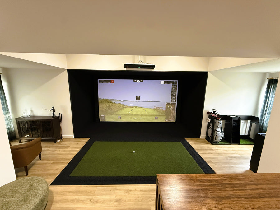 Golf simulator room with tables and chairs for seating behind it. Screen showing a golf round.