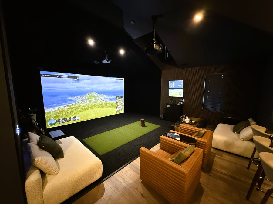 Indoor golf simulator setup with large screen displaying a golf game, surrounded by comfortable seating.