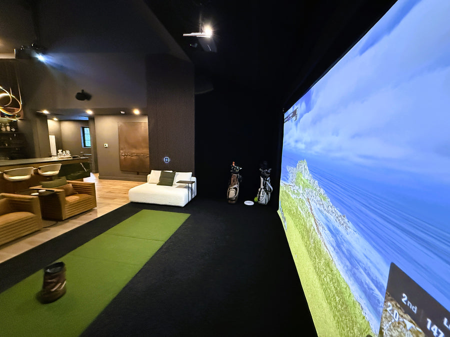 Indoor golf simulator setup in a modern living room with a large screen displaying a golf course.
