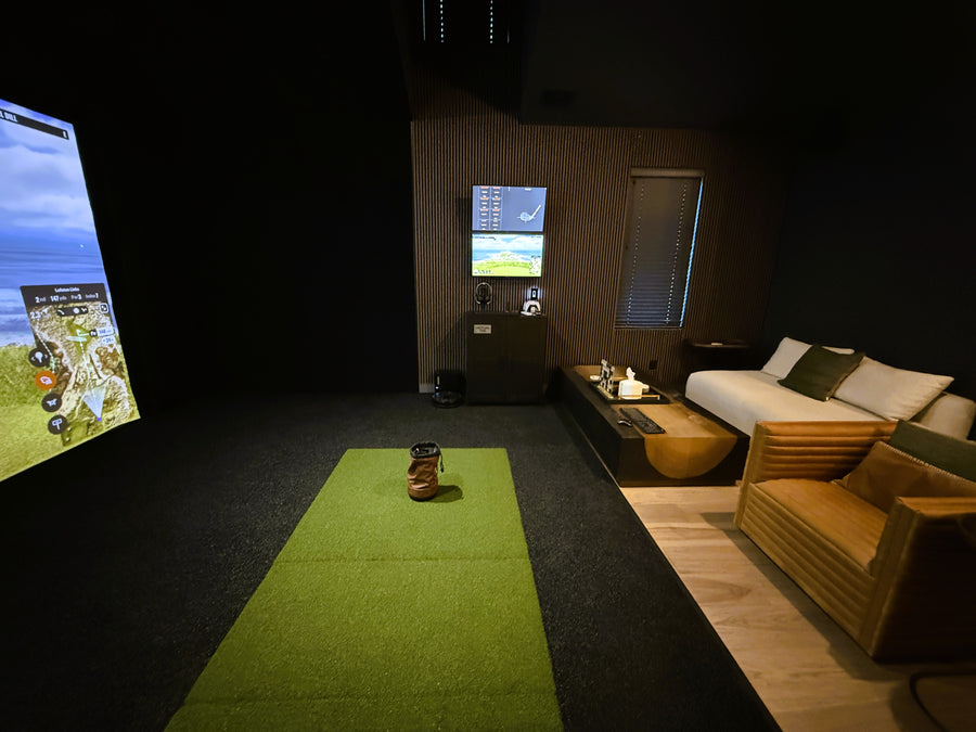 Indoor golf simulator with simulator screen and seating area in a dark room
