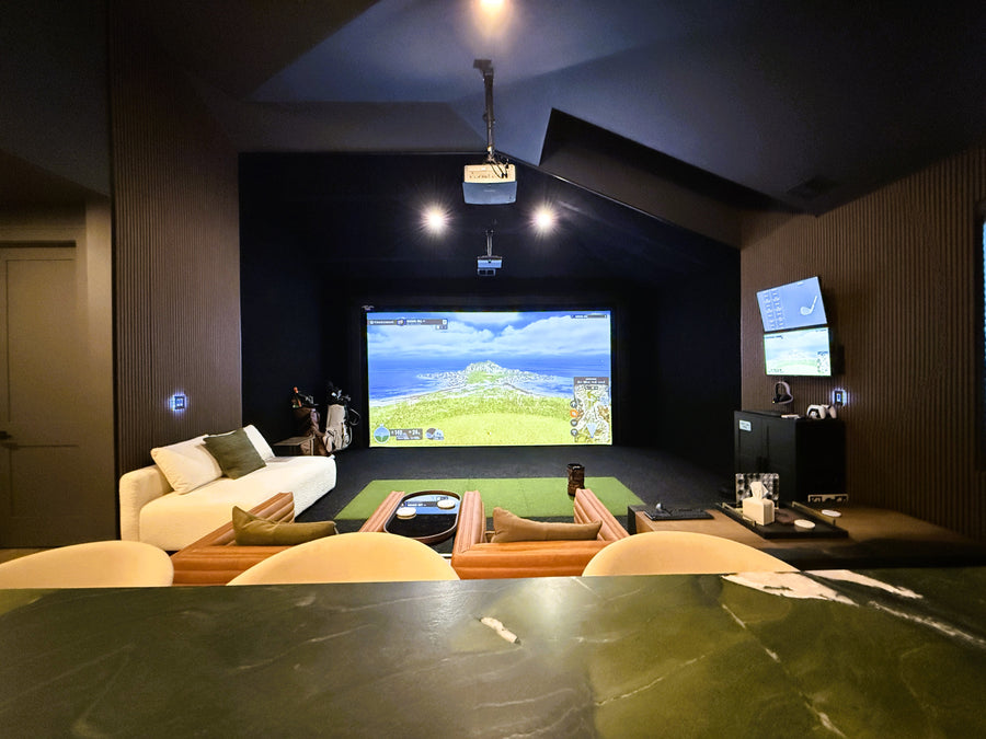 Indoor golf simulator with a large screen displaying a video game, surrounded by comfortable seating and entertainment equipment.