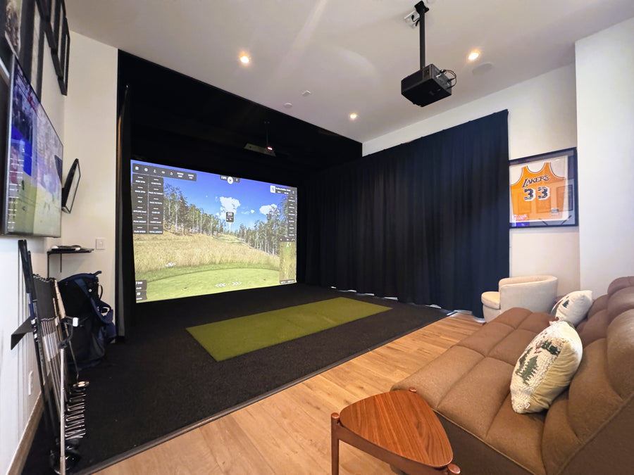 Indoor golf simulator room with a large screen displaying a golf simulation game, surrounded by furniture.
