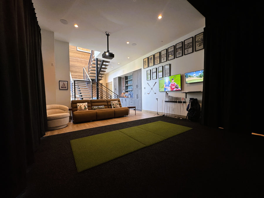 Modern golf simulator room with brown sofa, green rug, and wall art.