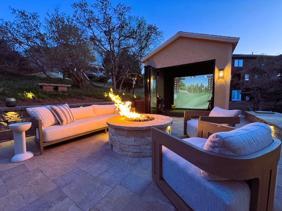 Outdoor patio with fire pit, seating area, and golf simulator in a shed display a golf game.