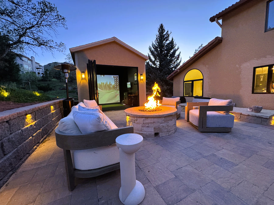 Outdoor patio with fire pit, seating area, and golf simulator shed at dusk.