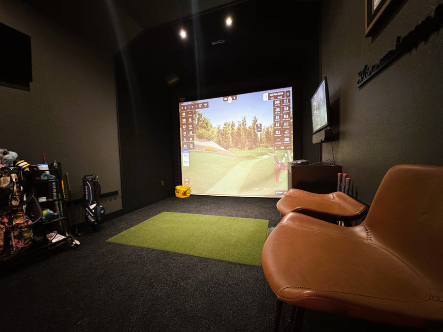 Golf simulator setup with a screen displaying a golf game, surrounded by golfing equipment.