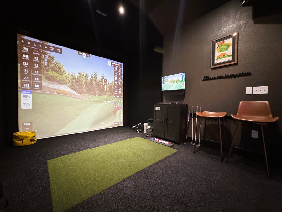 Indoor golf simulator setup with large screen and chairs in a room.
