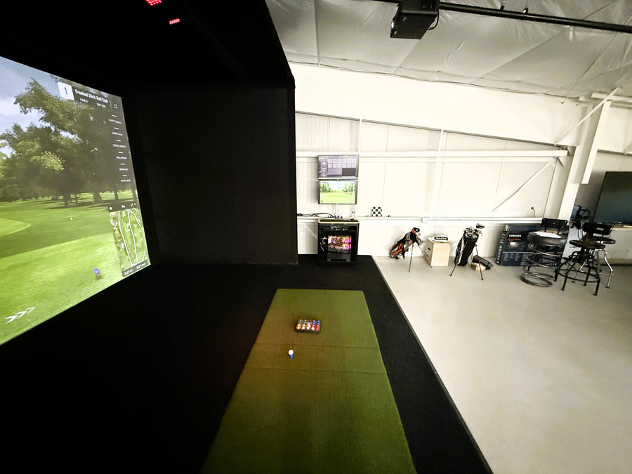 Golf simulator setup in a room with a large screen displaying a golf course.