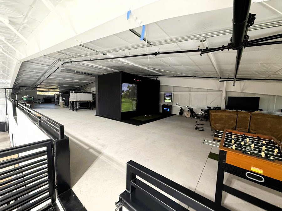 Indoor golf simulator area with a foosball table, TV, and sports simulator.