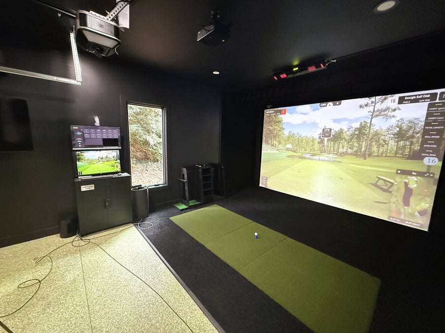 Golf simulator room with projection screen and interactive console.