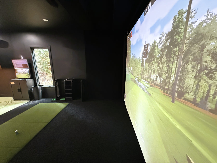 Indoor golf simulator setup with screen displaying a golf course.