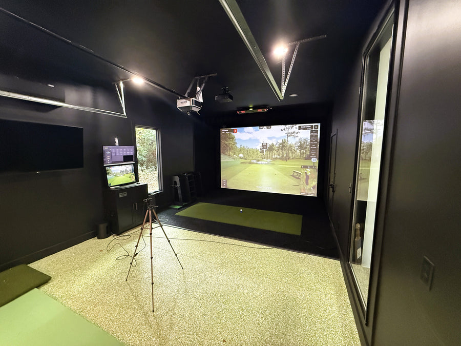 Indoor golf simulator setup with multiple screens and a green floor.