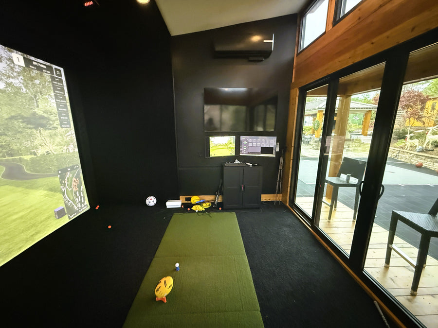 Indoor golf simulator room with large screen and multiple monitors.