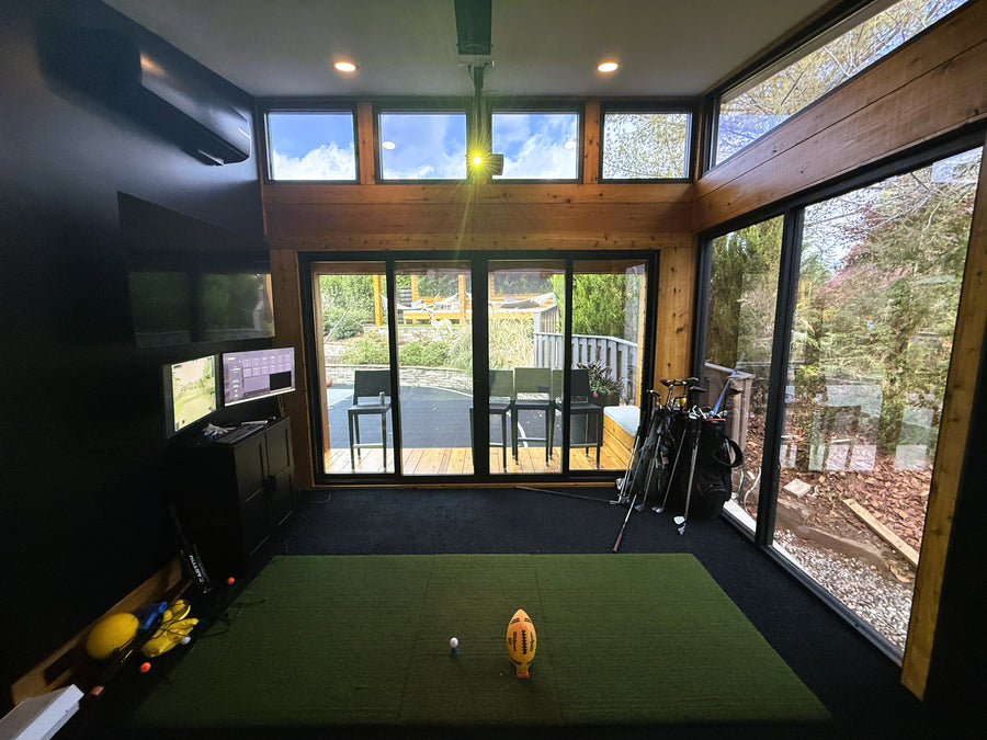 Indoor golf simulator room with green turf and TV screens.
