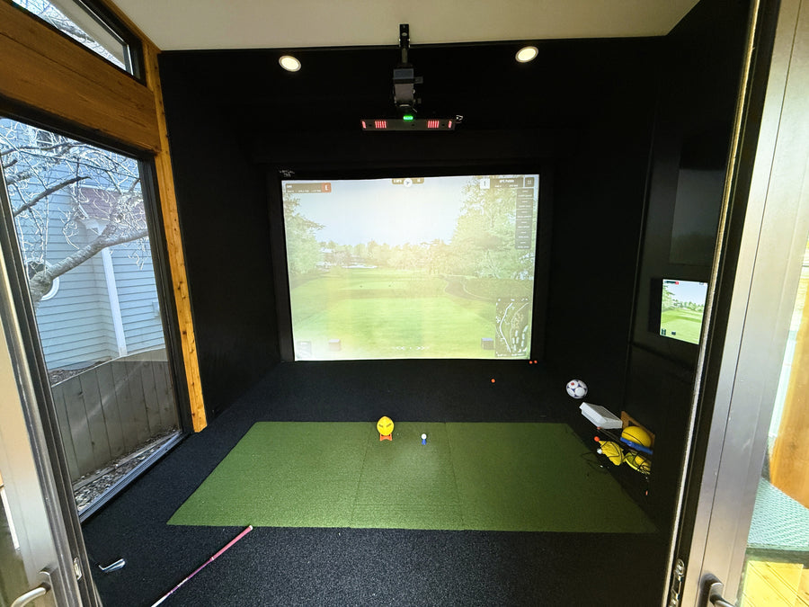 Indoor golf simulator setup with screen displaying a golf course.
