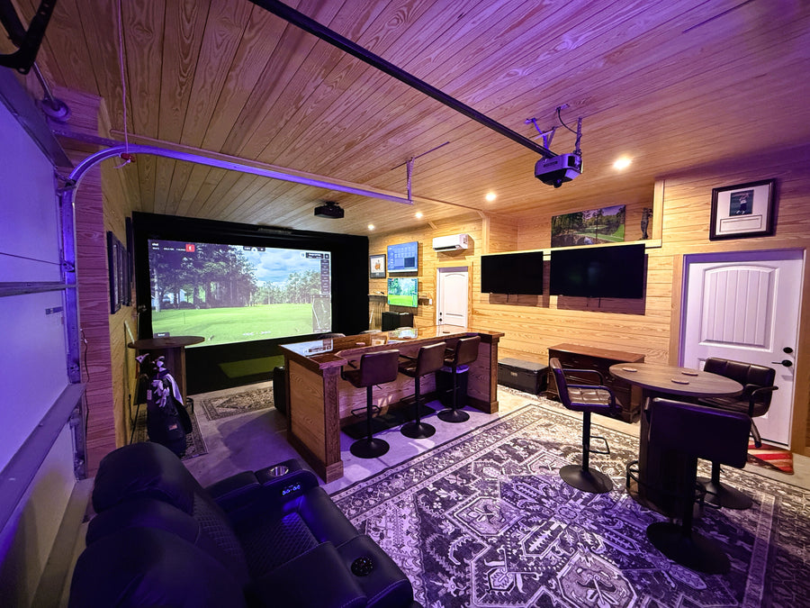 Golf simulator with multiple TV screens, gaming console, and comfortable seating.