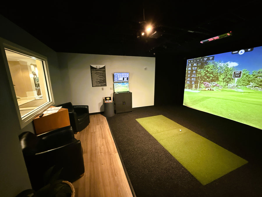 Indoor golf simulator room with screen displaying a golf course.