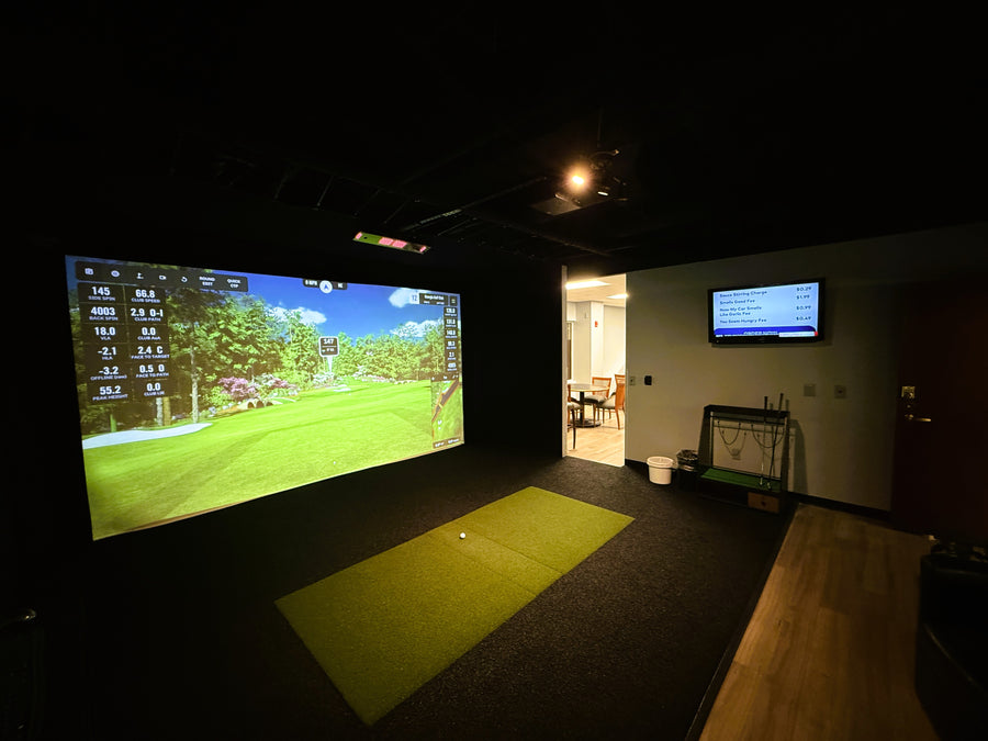 Indoor golf simulator setup with large screen displaying a golf course.