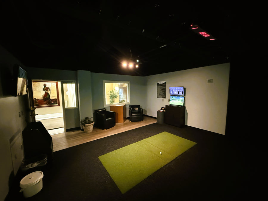 Golf simulator setup in a room with a green mat and TV screen.