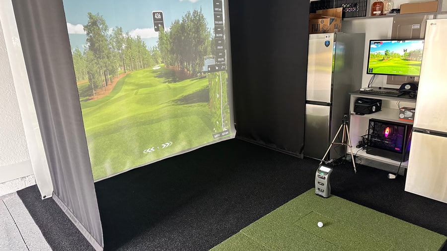 Indoor golf simulator setup with screen displaying a golf course, surrounded by household appliances.