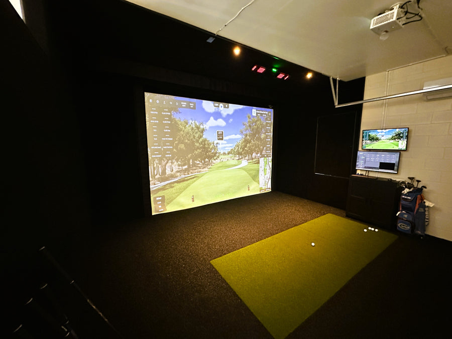 Indoor golf simulator setup with projection screen and equipment.