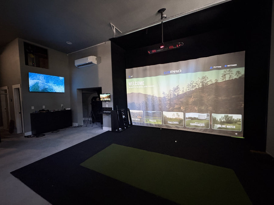 Garage with golf simulator and the screen displaying GSPro software. Green and black turf on the ground. 