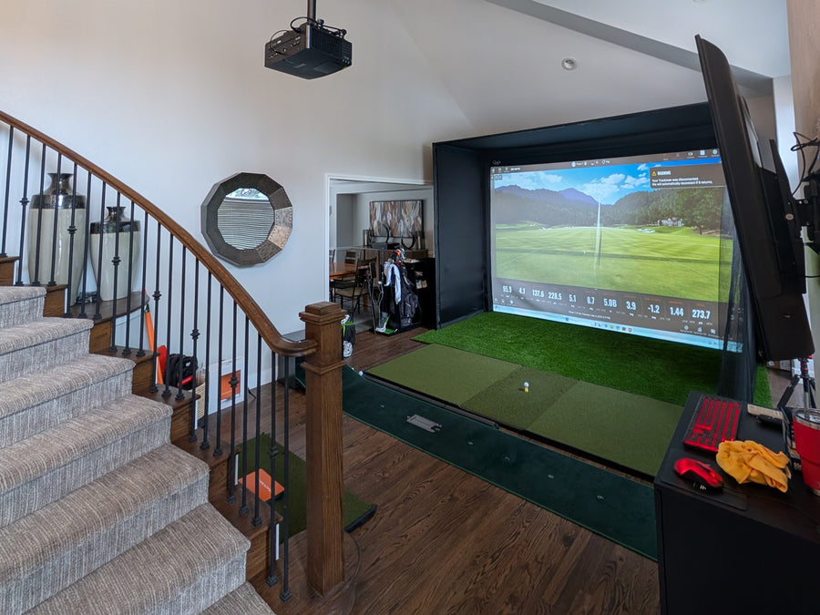 Indoor golf simulator setup in a home with a large screen and projector.