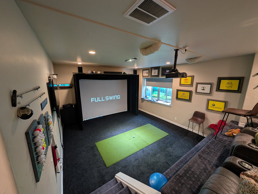 Indoor golf simulator setup in a living room with a screen displaying 'FULL SWING'.