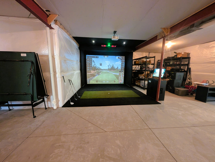 Indoor golf simulator setup in a garage with a screen displaying a golf course.