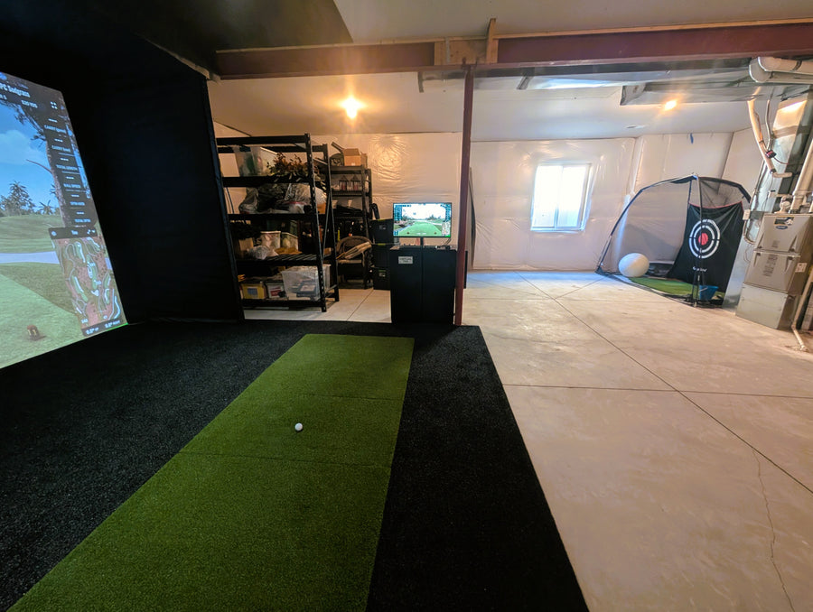 Indoor golf simulator setup in a home garage with a screen displaying a golf course.