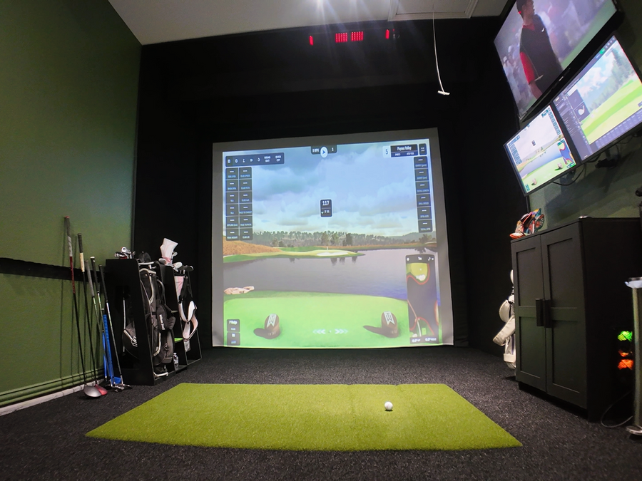 Golf simulator setup with multiple screens and golf equipment in a room.