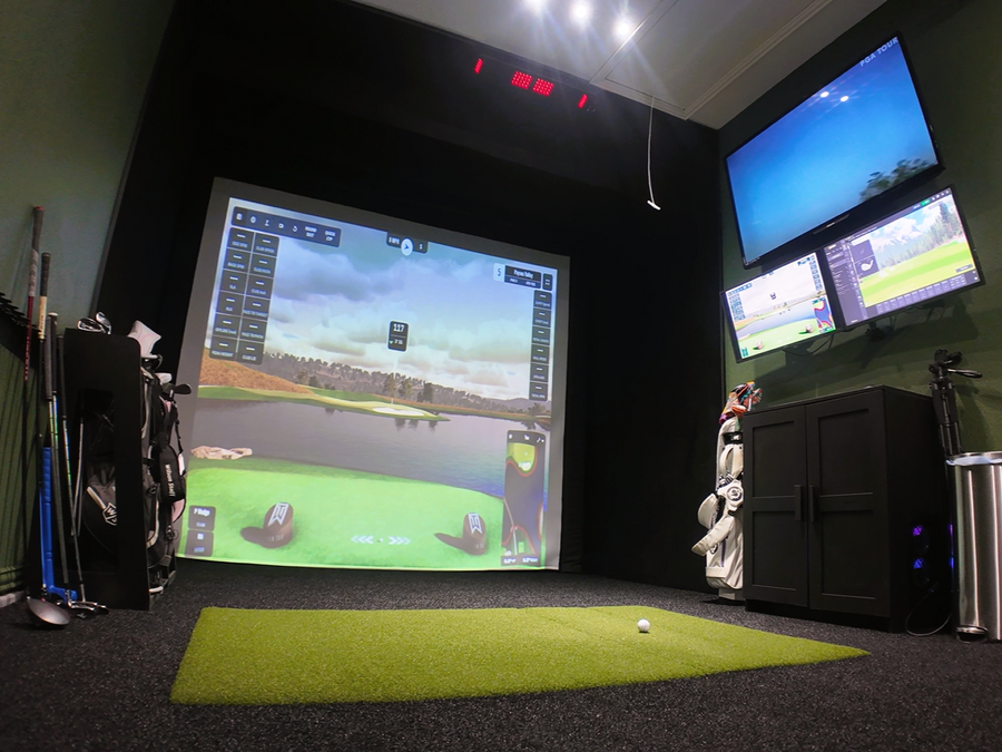 Golf simulator setup with multiple screens and golf equipment in a room.