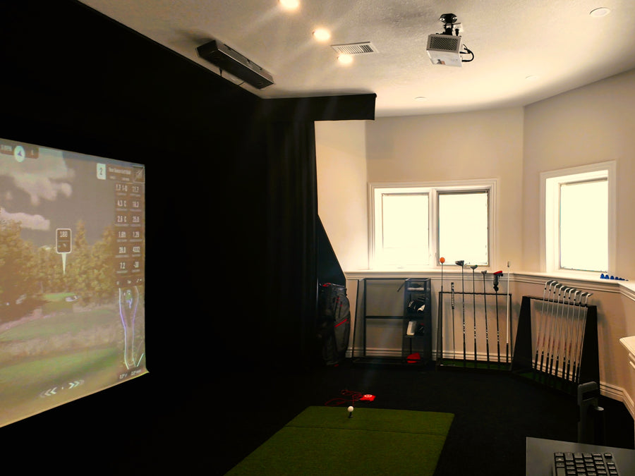 Indoor golf simulator setup with projector and screen in a room with windows.
