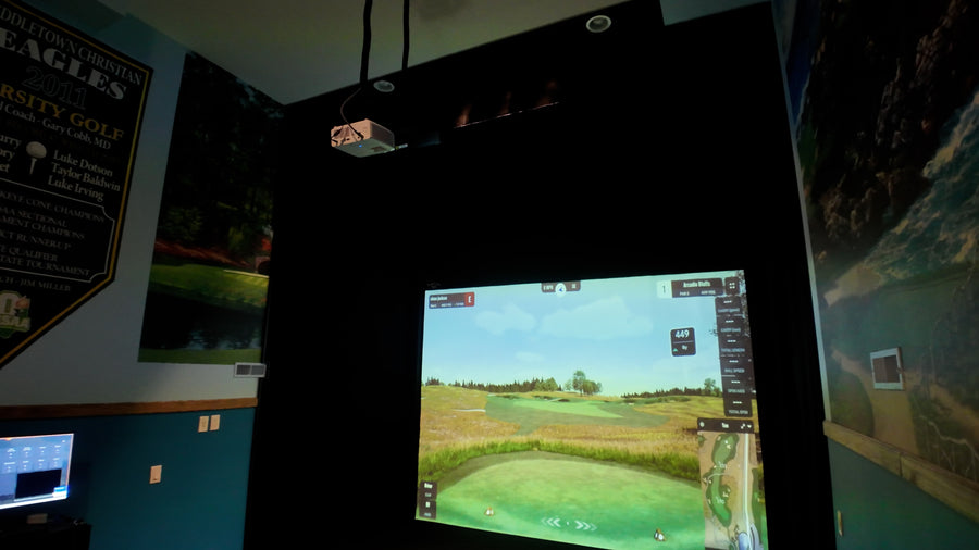 Golf simulator setup in a room with a screen displaying a golf course.
