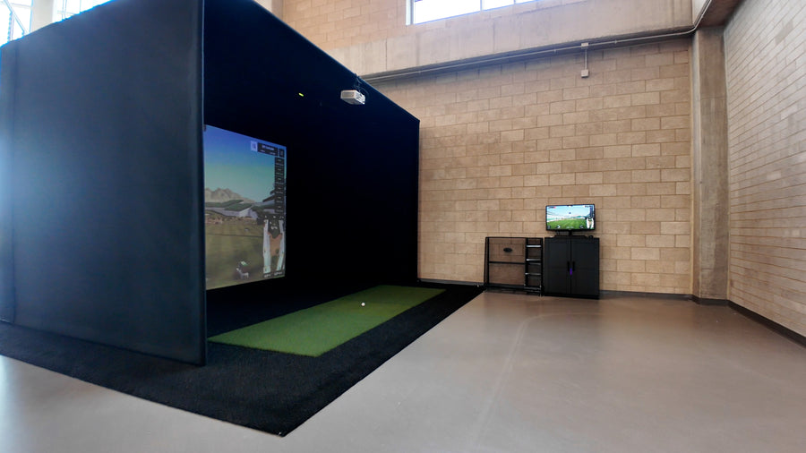 Indoor golf simulator setup in a room with brick walls and a small TV.