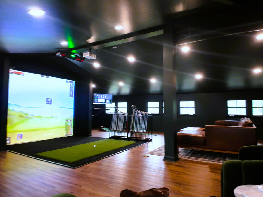Indoor golf simulator setup in a living room with a large screen and golf simulator equipment.