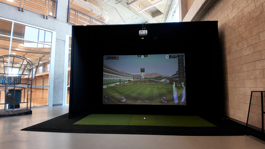 Golf simulator setup in a modern indoor facility with a screen displaying a golf course.