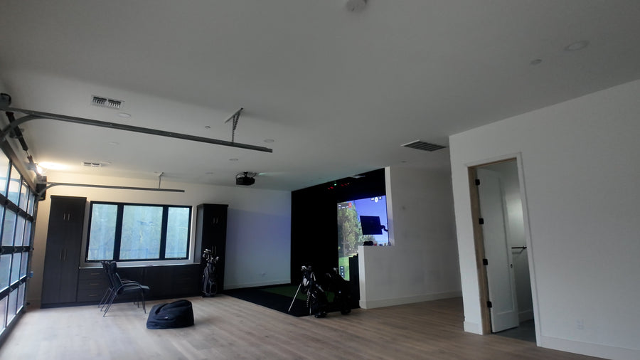Golf simulator space with large windows, white walls, and minimal furniture.
