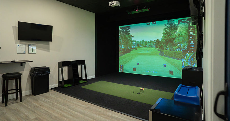 Indoor golf simulator setup in a room with a screen displaying a golf course.