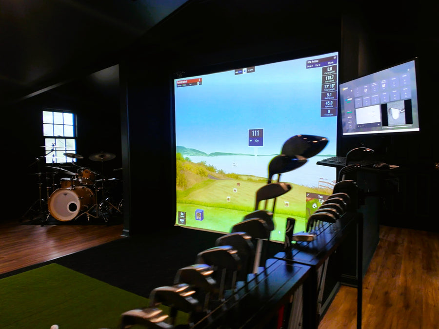 Golf simulator setup with screen displaying a golf course and multiple golf clubs on a stand.