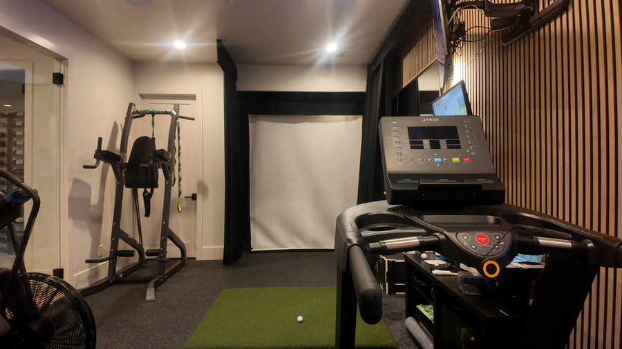 Gym golf simulator room with treadmill, weight machine, and exercise ball.